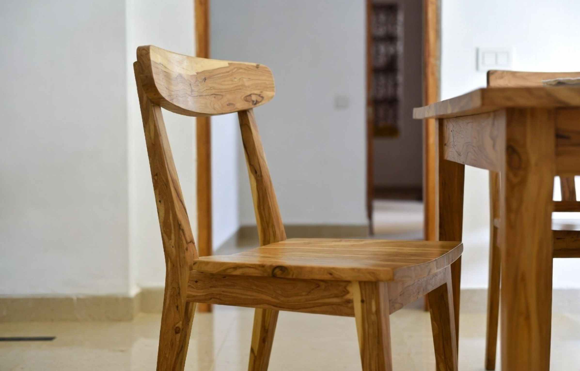 Wooden dining chair with a curved backrest, placed beside a table in a minimalist indoor setting.